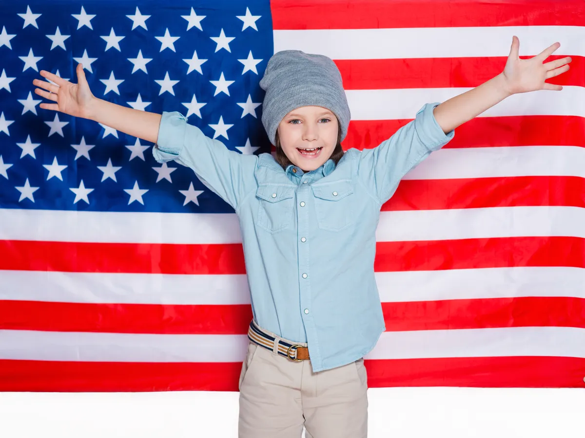 Happy young boy smiling in front of American flag representing US citizenship for minors
