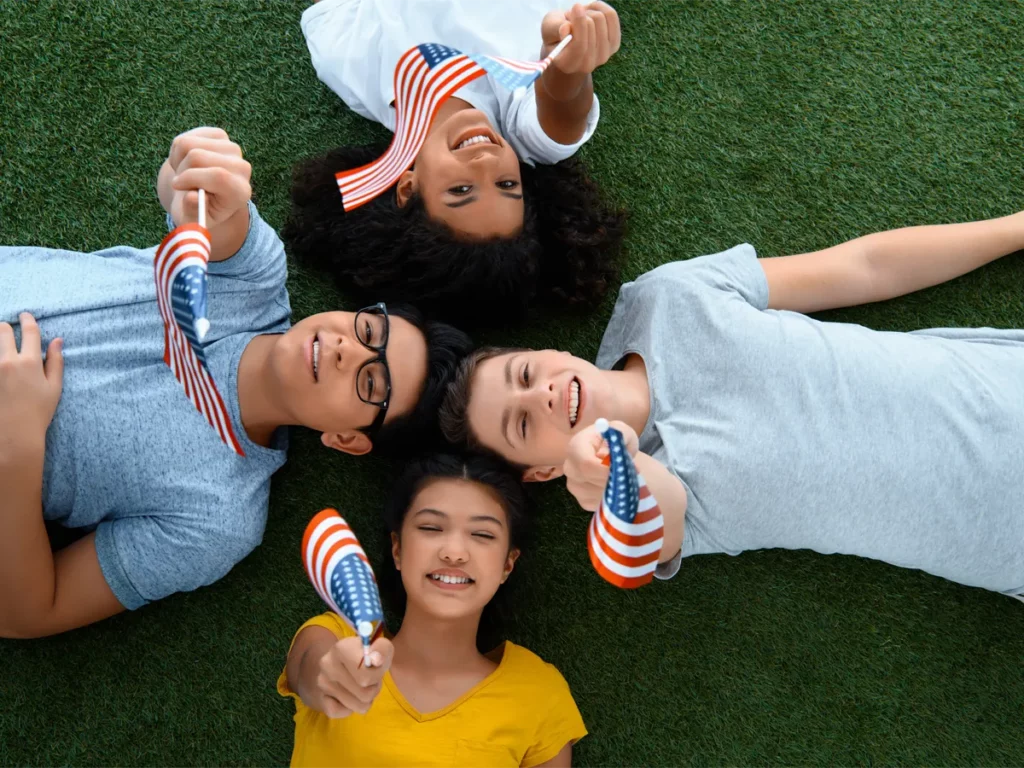 Smiling teens outside the US holding American flags, hoping for US citizenship for minors